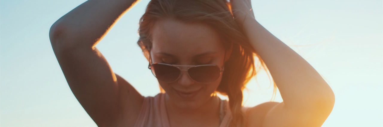 A woman at the beach at sunset, wearing sunglasses, looking down