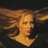 A blond woman wearing black, lifting her hair up