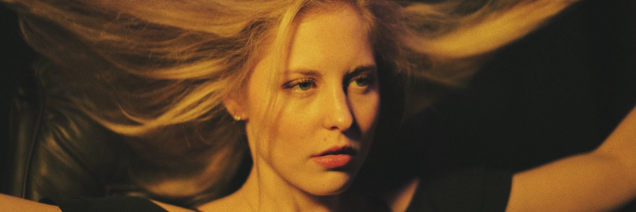 Why I Understand Suicide Contagion After My Friend Killed Himself A blond woman wearing black, lifting her hair up