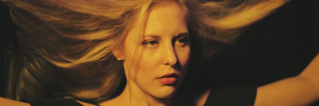 A blond woman wearing black, lifting her hair up