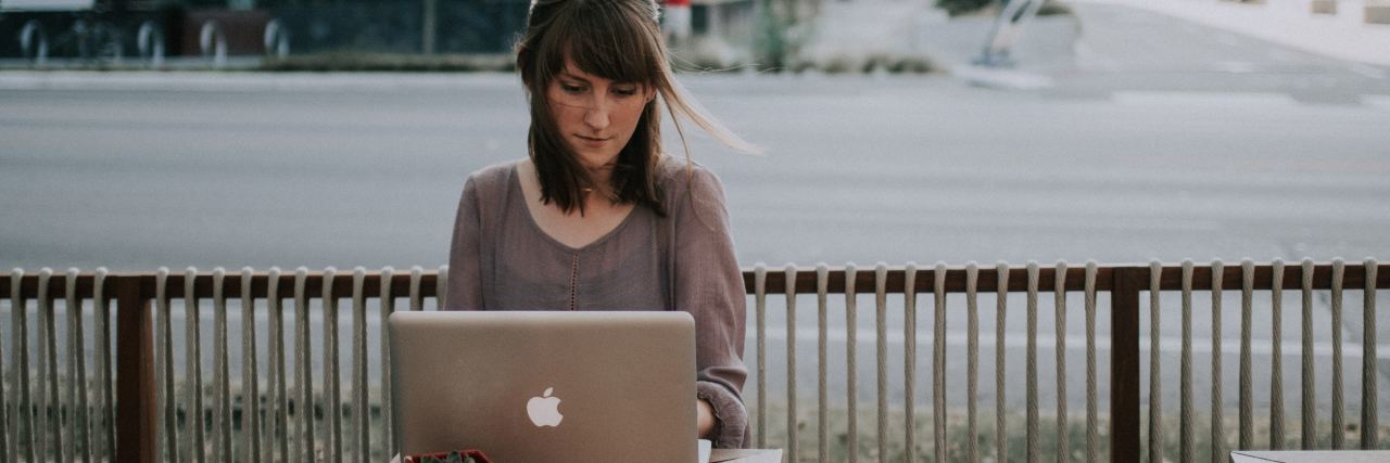 photo of woman writing on laptop outside coffee shop with road behind her