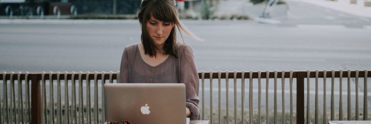How Writing About Mental Health Makes a Difference photo of woman writing on laptop outside coffee shop with road behind her