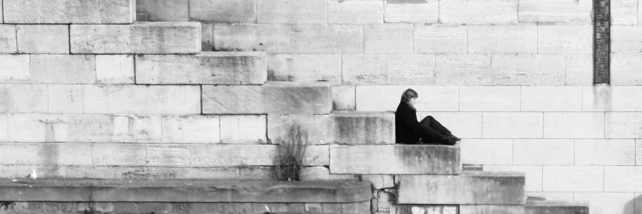 Self-Isolation and Emotionally Abusive Partners black and white photo of woman sitting on stone steps by ocean alone