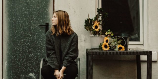 The Loneliness You Experience With Endometriosis photo of young woman sitting outside cottage with sunflowers on small table nearby