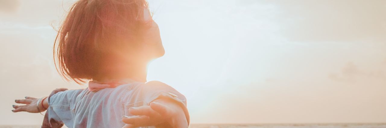 How to Relax With Chronic Tension and Chronic Pain photo of woman at sunrise or sunset with arms outstretched behind her in relaxation or happiness