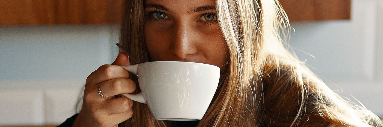 photo of young woman looking into camera with coffee cup raised to mouth