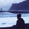 photo of man looking out to rough ocean and rocky coast