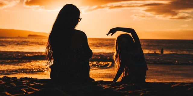 photo of mother and daughter silhouetted against sunset on beach in front of ocean