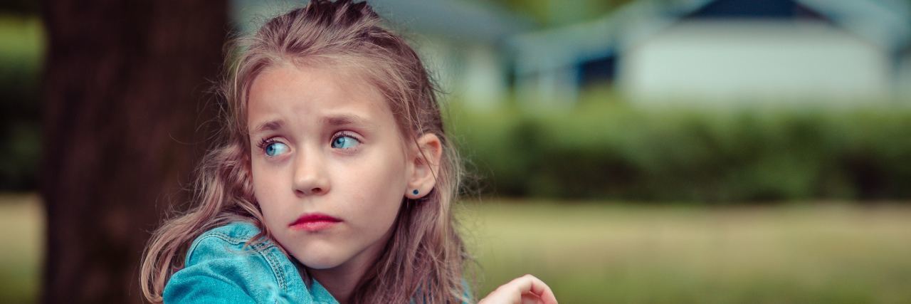 KHN: The Long and Winding Road to Mental Health Care for Your Kid Blinde-haired, blue-eyed young girl sitting on the grass wearing denim