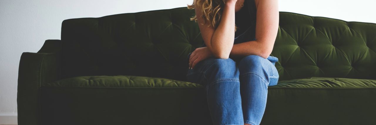 Talking Therapy Helped Me Come to Terms With My Chronic Fatigue photo of woman sitting on green sofa with elbow resting on leg. she is bare-footed and her head can't be seen