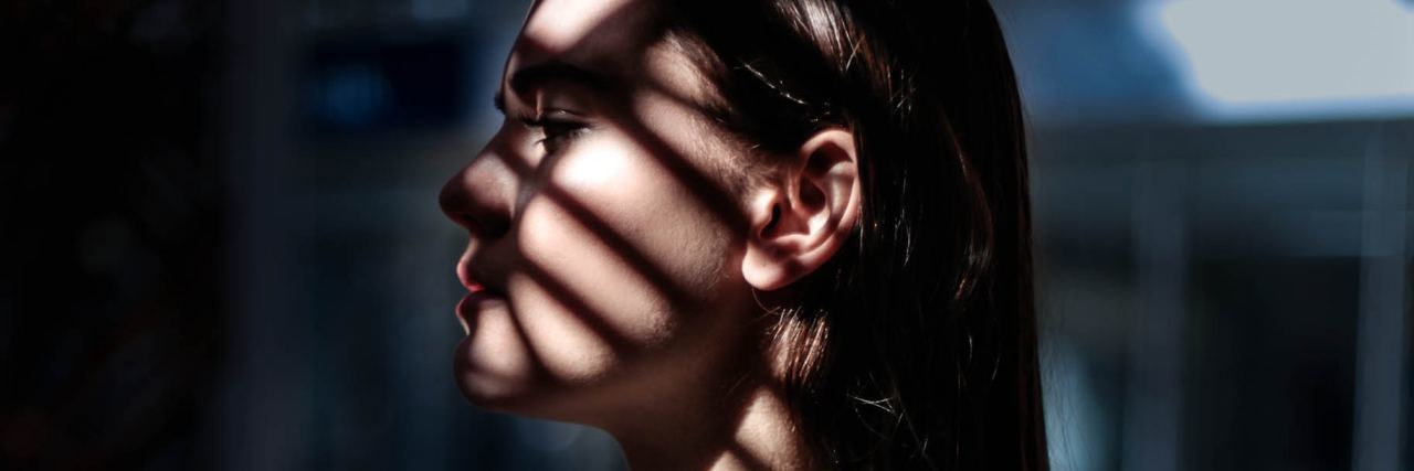 My Eating Disorder Is Like an Emotionally Abusive Relationship photo of woman with dark hair partly silhouetted by light through window