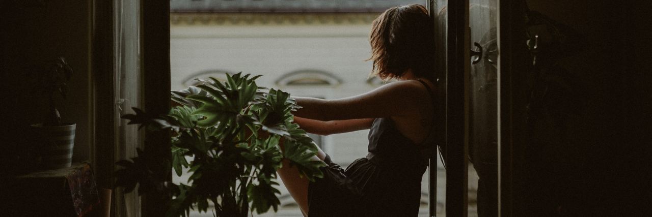 photo of woman sitting by open window looking out over rooftops