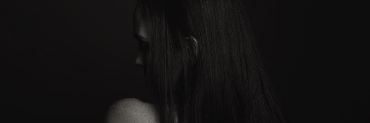 black and white photo of young woman, from behind, hiding face and looking sad with only her shoulder visible