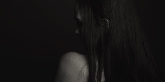 black and white photo of young woman, from behind, hiding face and looking sad with only her shoulder visible