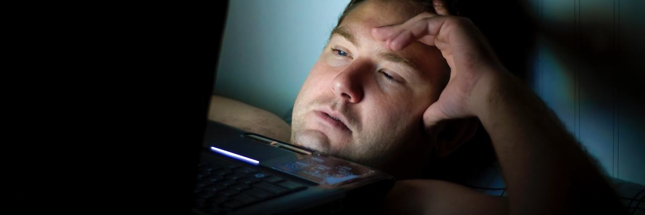 photo of man unable to sleep at night with laptop balanced on chest