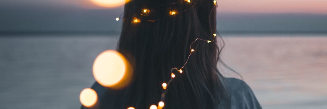 photo of woman looking out at lake with fairy lights leading from camera to her hair