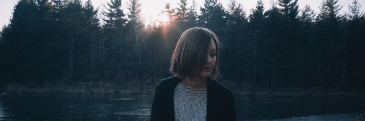 photo of woman at unset standing in front of lake and forest