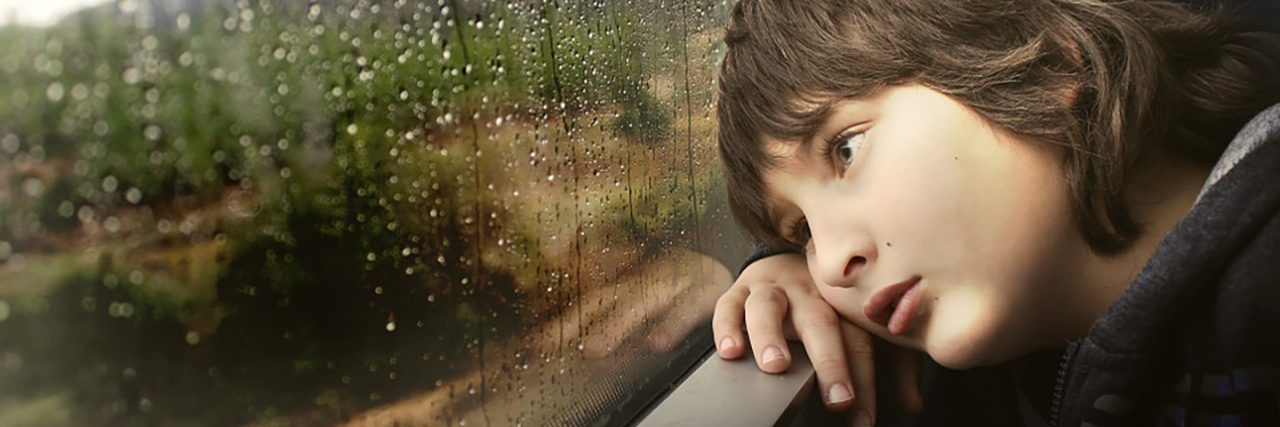 Boy looking sadly out window.