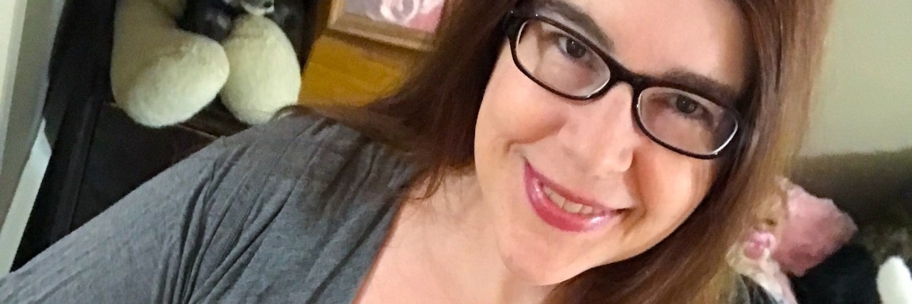 A woman with glasses is smiling at the camera.