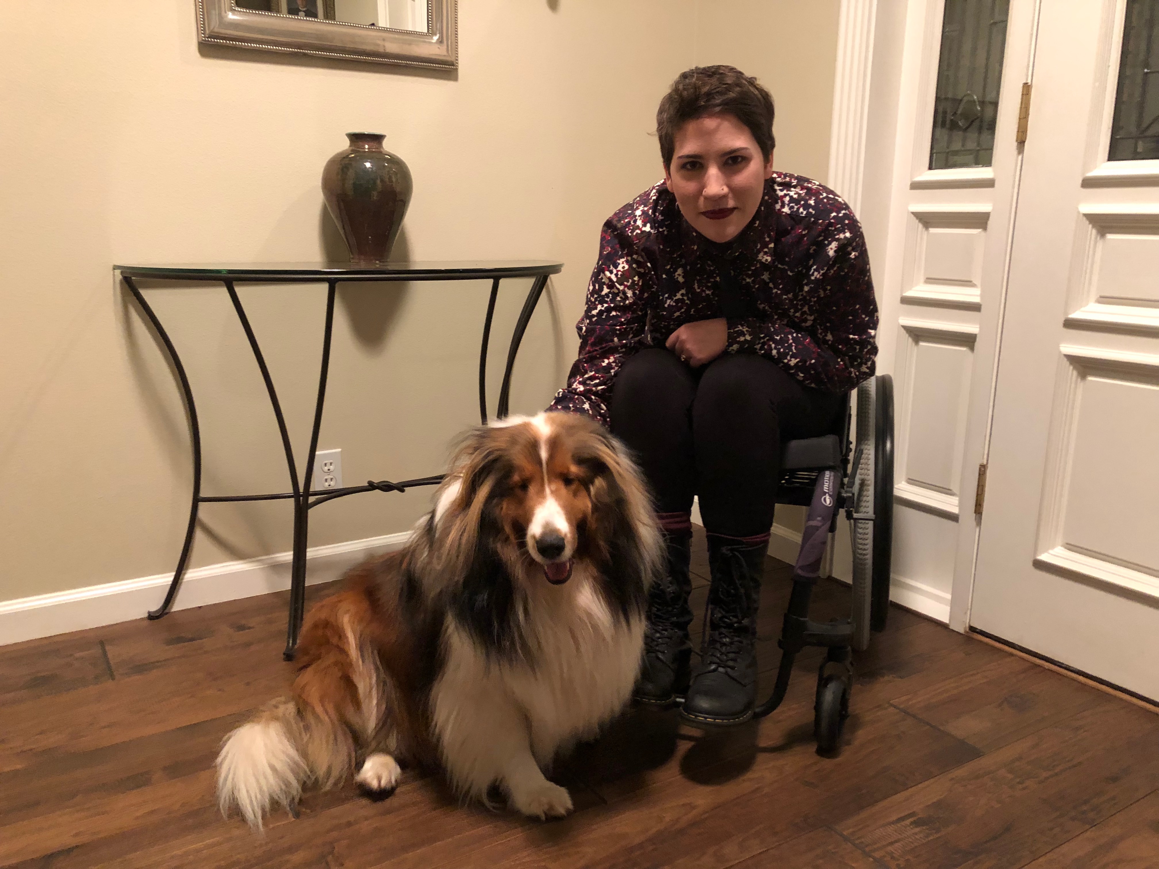 Ellery sitting in a wheelchair with a collie dog sitting at their feet.