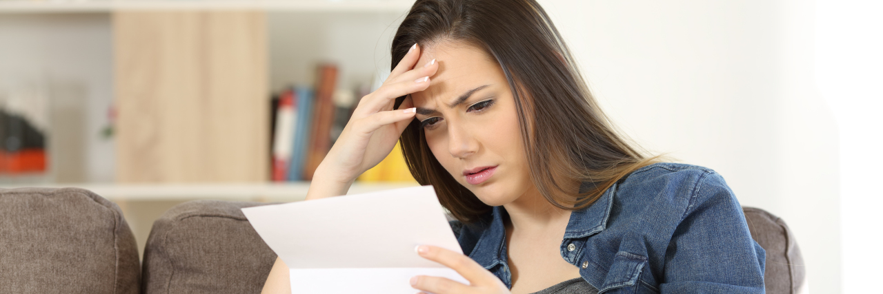 Giving Up the Fight for Disability Benefits: What It's Like Concerned woman reading bad news in a letter sitting on a couch in the living room at home