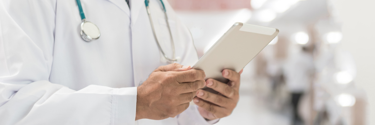 To the ER Doctor Who Insulted Me for Being On Disability Benefits Doctor in hospital holding tablet.