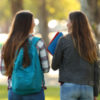 Back view of two happy students walking and talking in a university campus
