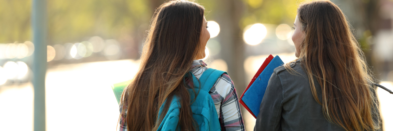 Back view of two happy students walking and talking in a university campus