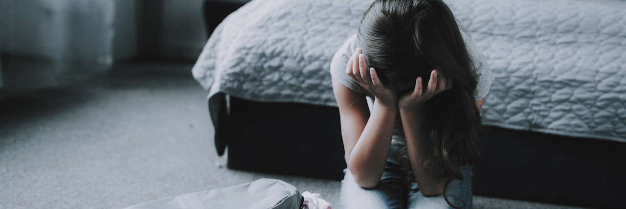 How Adoption Can Hurt Someone's Mental Health A young girl sitting in front of her bed, holding her head in her hands, looking distressed