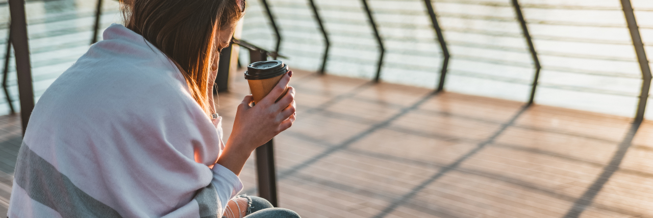 How Life Changes After a Chronic Illness Diagnosis woman sitting with blanket near the water, holding coffee