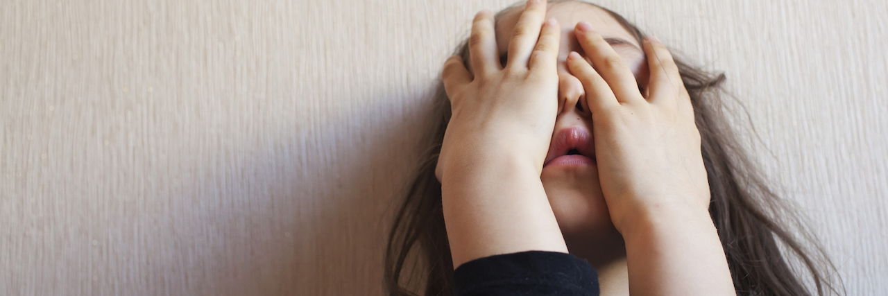 How the Mental Health System Fails Kids With Behavioral Problems Little girl covers her face with her hands