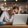 a young woman looking sad working on a laptop at a coffee shop