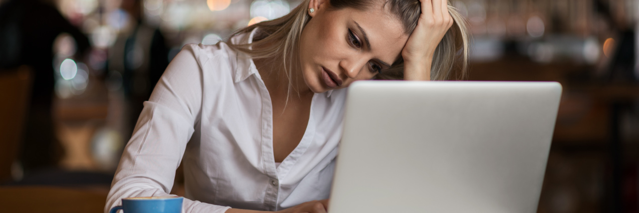 What It's Like to Live in a Depressed State of Mind a young woman looking sad working on a laptop at a coffee shop