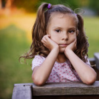 A young girl with pigtails resting her head on her hands