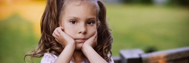 A young girl with pigtails resting her head on her hands