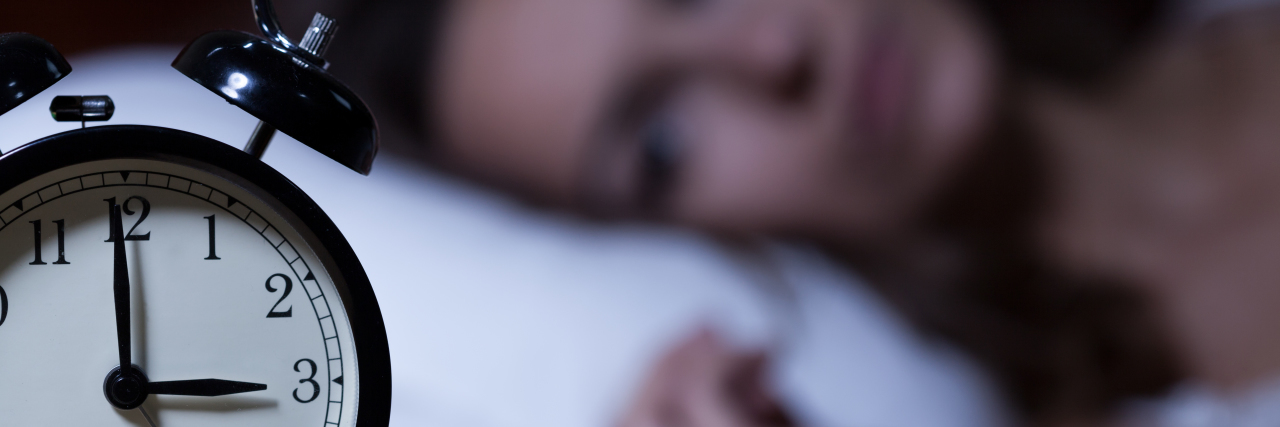 How My Eating Disorder Became an Alarm System A woman staring at an alarm clock from her bed