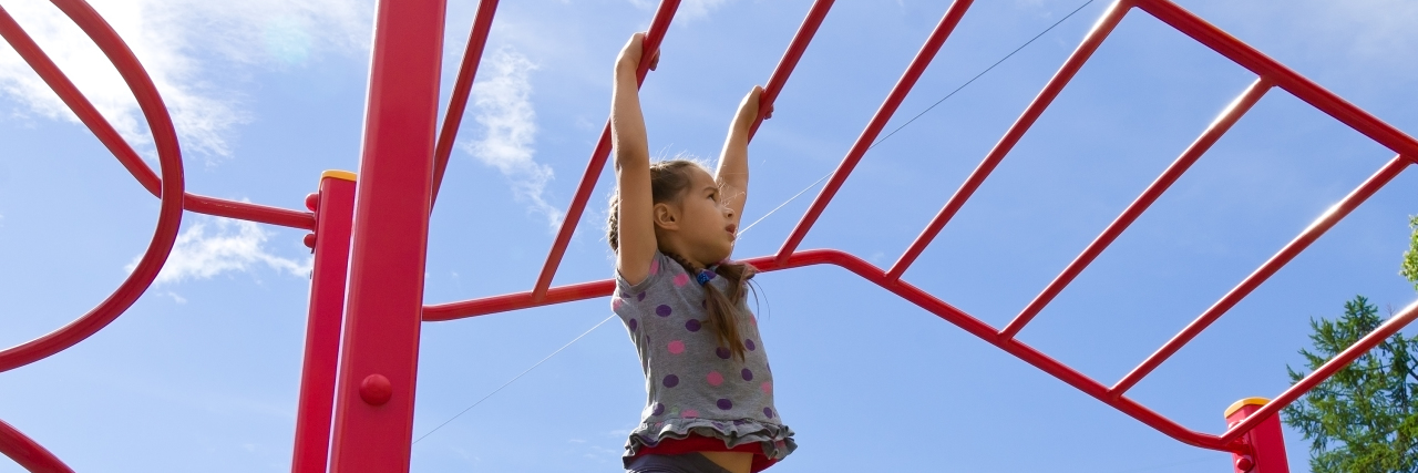 How Undiagnosed Chronic Illness Can Affect Self-Esteem Little girl playing on monkey bars.