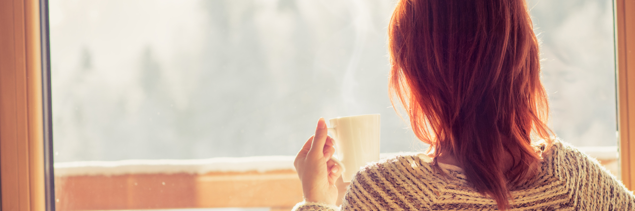 a woman is sitting on a chair, drinking coffee and staring out the window.