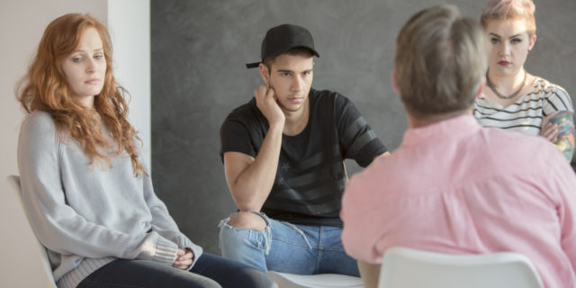 photo of group therapy session with multiple young people talking to older male therapist
