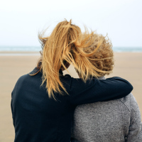 Back view of senior and young woman looking at sea on the beach in autumn