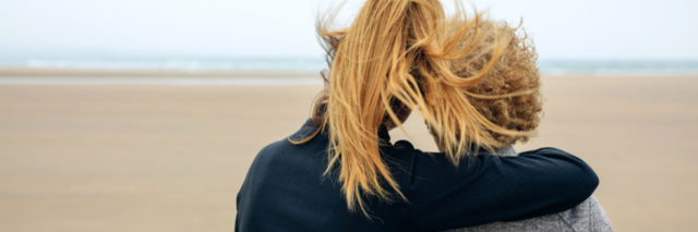 Back view of senior and young woman looking at sea on the beach in autumn