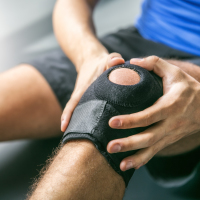 close up photo of man with knee brace holding knee in pain