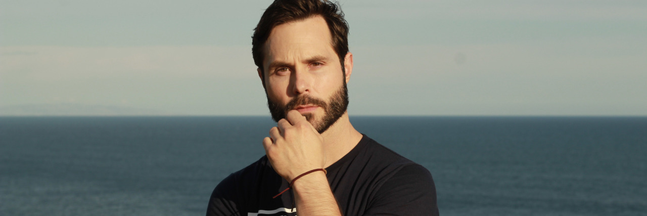 How My Mom Saved My Life When I Was a Suicidal Teen A man is posing for the camera while standing in front of a large body of water.