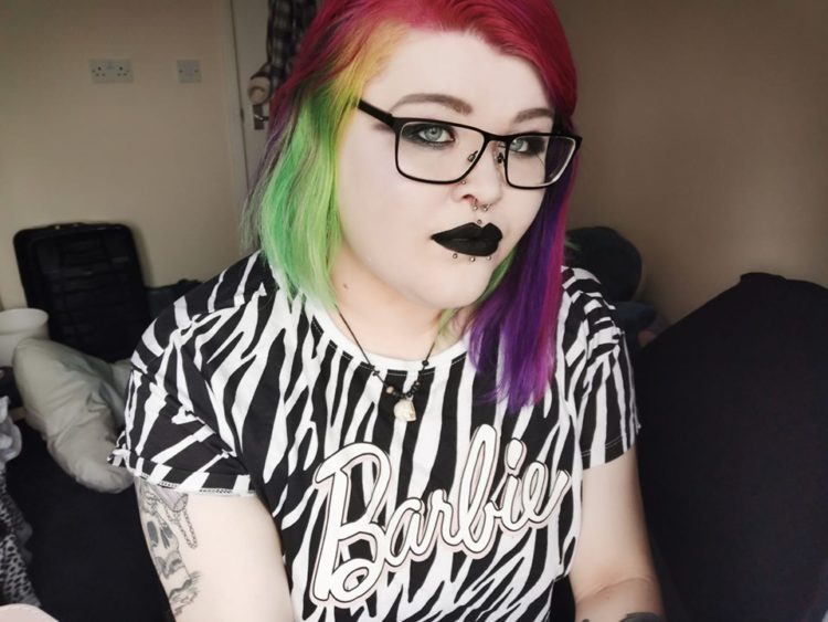 woman with pink, yellow, green and purple hair. Wearing black lipstick and a zebra "barbie" shirt