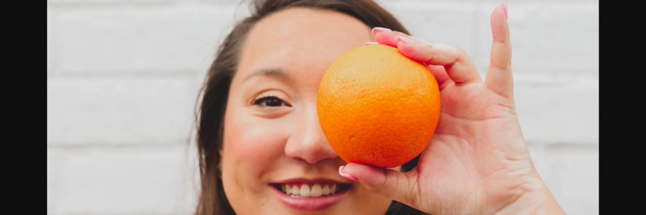 Woman smiling and holding an orange over her eye