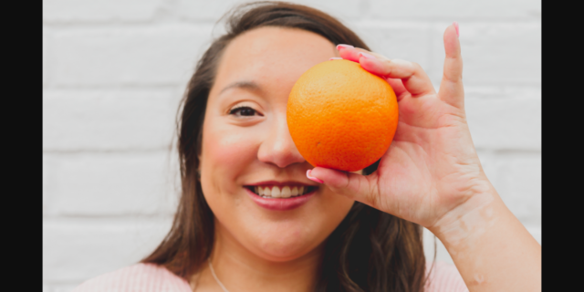 Woman smiling and holding an orange over her eye