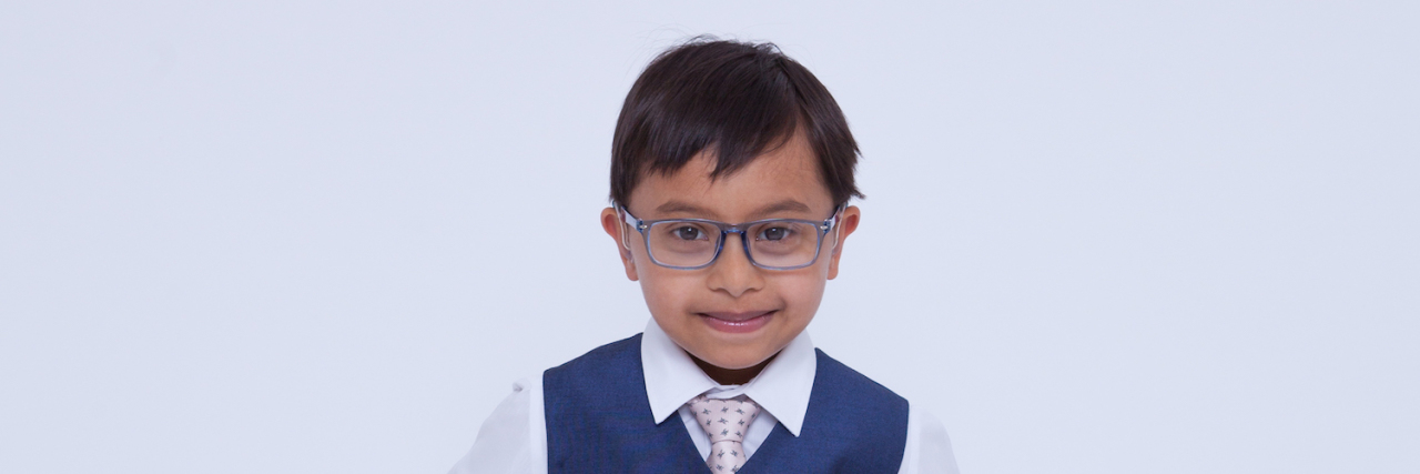 Being a Pediatrician Who Has a Baby With Down Syndrome Little boy with Down syndrome looking sharp wearing a suit, hands on hips.
