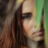 photo of redhead woman standing behind leaves looking serious into camera