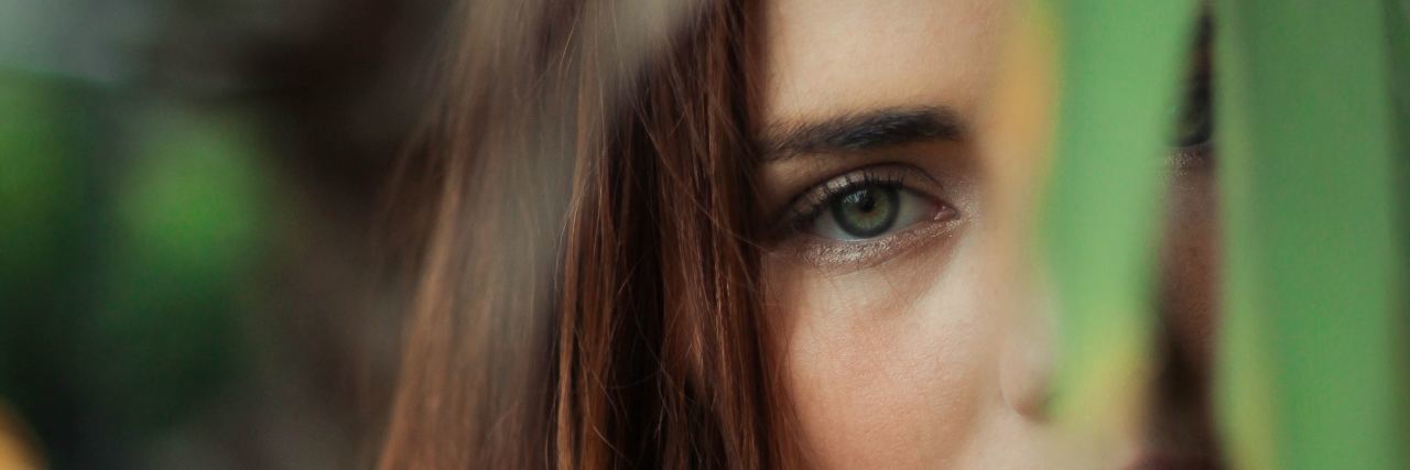 How to Offer Advice to Someone With Chronic Pain photo of redhead woman standing behind leaves looking serious into camera