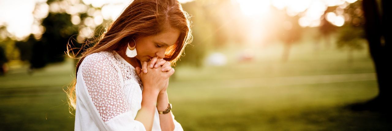 photo of young woman in countryside with head bowed in prayer